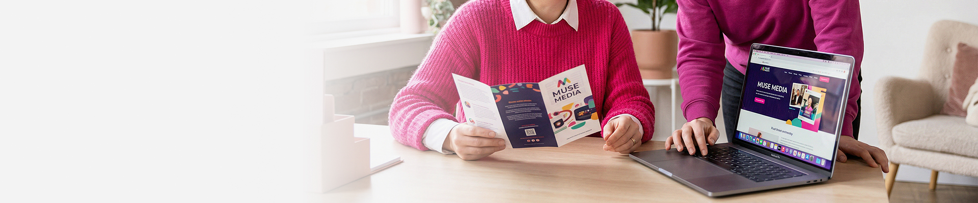 Zwei Personen vergleichen einen gedruckten Flyer mit der zugehörigen Webseite auf einem Laptop.