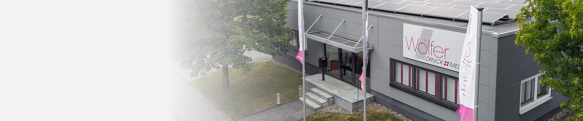 Gebäude von Wölfer Druck+Media mit Firmenschild, Fahnen und Solaranlage auf dem Dach.