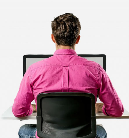 Mitarbeiter im pinken Hemd sitzt am Computer und arbeitet an Agenturleistungen.