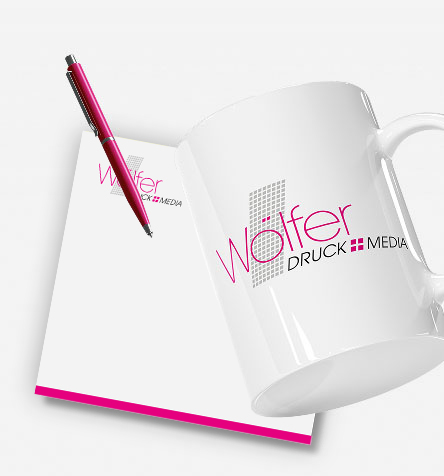 Weiße Tasse, Notizblock und pinker Kugelschreiber als Werbemittel mit Logo von Wölfer Druck+Media.